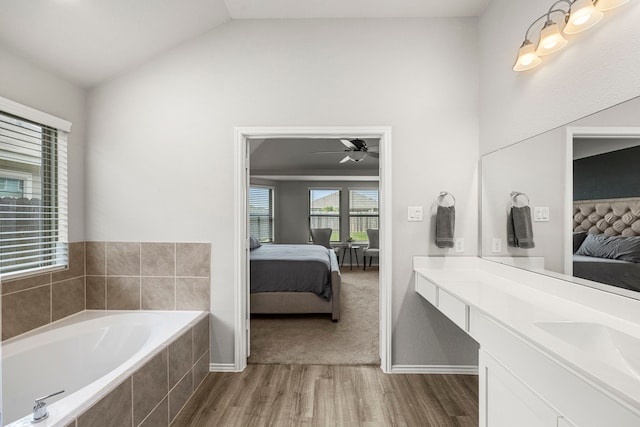 bathroom featuring hardwood / wood-style floors, lofted ceiling, vanity, a relaxing tiled tub, and ceiling fan