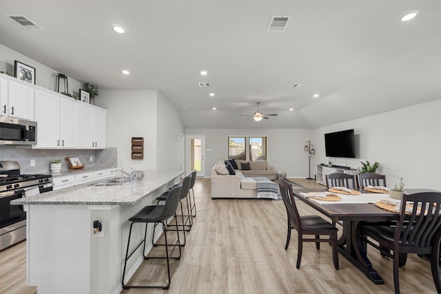 kitchen featuring sink, appliances with stainless steel finishes, an island with sink, white cabinets, and a kitchen bar