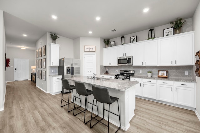 kitchen with white cabinetry, sink, stainless steel appliances, light stone countertops, and a center island with sink