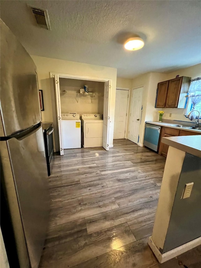 kitchen with sink, washer and clothes dryer, appliances with stainless steel finishes, light hardwood / wood-style floors, and a textured ceiling