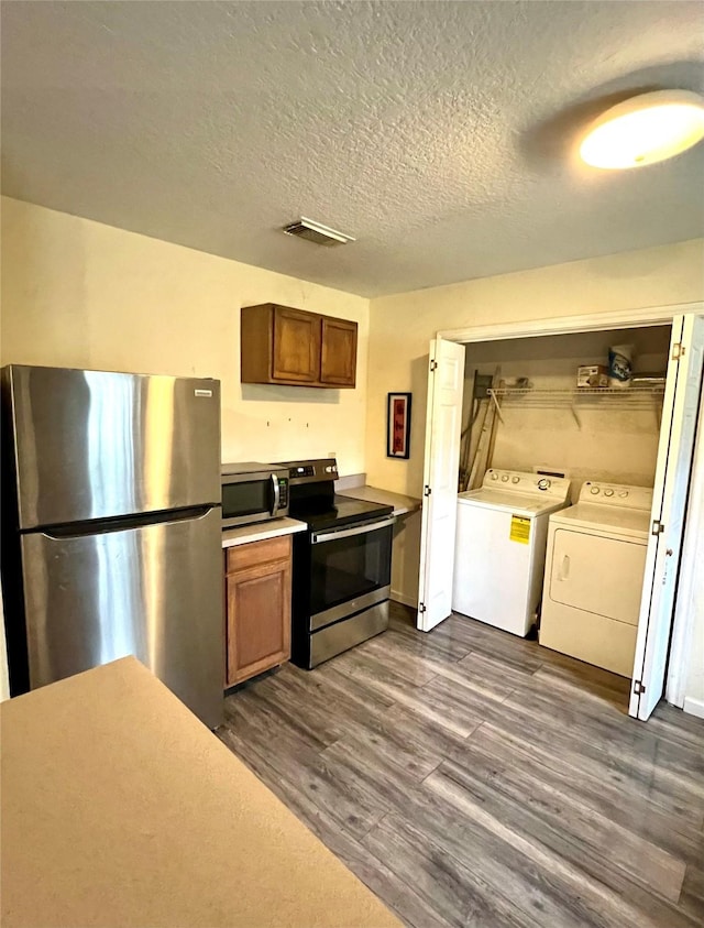 kitchen featuring dark wood-type flooring, washing machine and clothes dryer, appliances with stainless steel finishes, and a textured ceiling