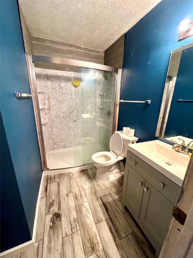 bathroom with vanity, toilet, a shower with shower door, and a textured ceiling