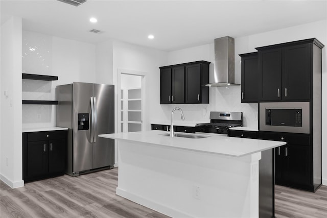 kitchen featuring appliances with stainless steel finishes, an island with sink, sink, light hardwood / wood-style floors, and wall chimney exhaust hood