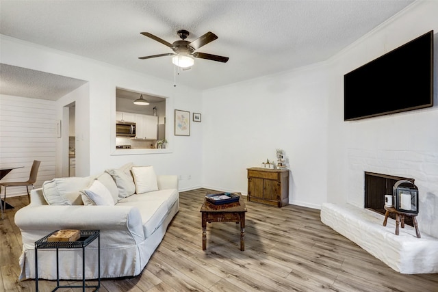 living room with ceiling fan, crown molding, light hardwood / wood-style floors, and a textured ceiling