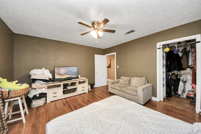 bedroom with dark wood-type flooring, a textured ceiling, ceiling fan, and a closet