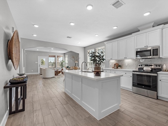 kitchen with sink, appliances with stainless steel finishes, white cabinets, a center island with sink, and decorative backsplash