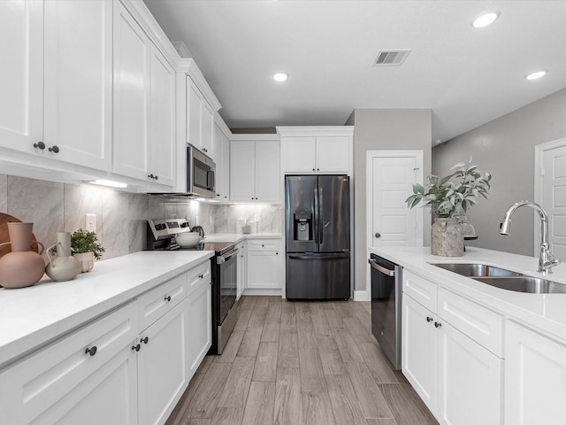 kitchen featuring tasteful backsplash, sink, white cabinets, stainless steel appliances, and light wood-type flooring