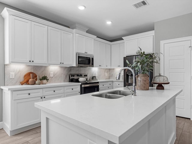 kitchen featuring sink, light hardwood / wood-style flooring, a kitchen island with sink, stainless steel appliances, and white cabinets