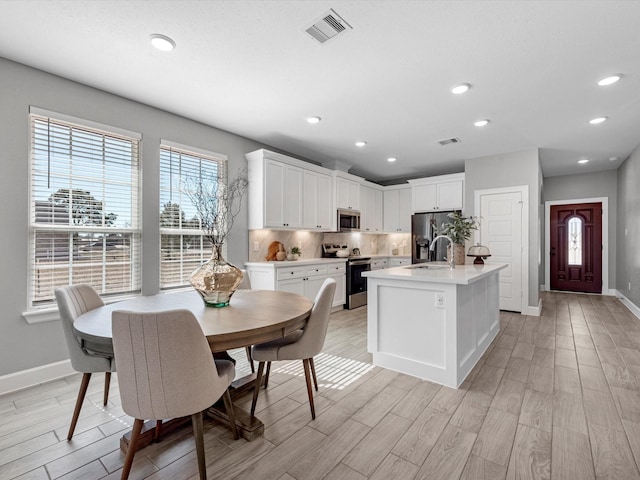 kitchen with white cabinetry, appliances with stainless steel finishes, an island with sink, and decorative backsplash