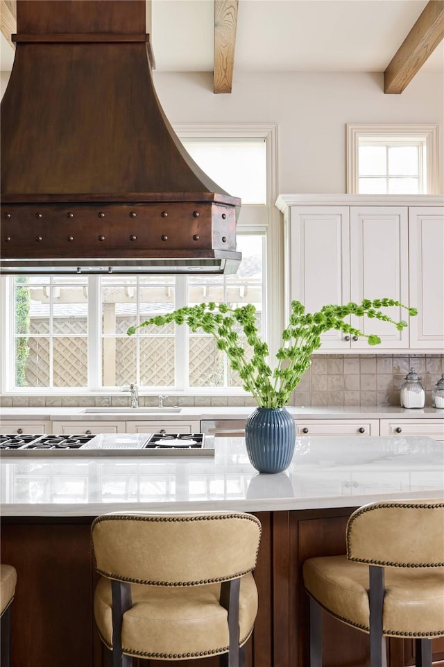 kitchen with beamed ceiling, sink, a breakfast bar area, custom exhaust hood, and gas stovetop