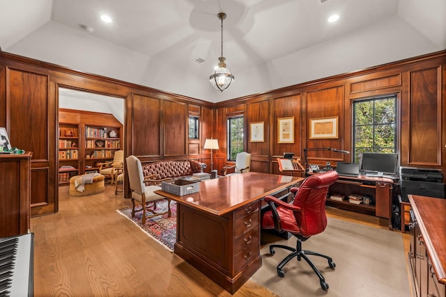 home office featuring built in shelves, a wealth of natural light, wood walls, and light hardwood / wood-style flooring