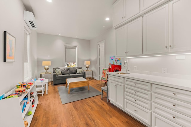 kitchen with sink, a wall mounted AC, white cabinets, and light wood-type flooring