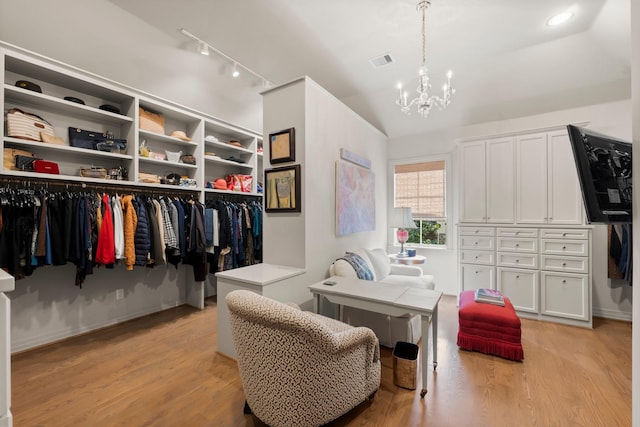 walk in closet featuring vaulted ceiling, light hardwood / wood-style floors, and a notable chandelier