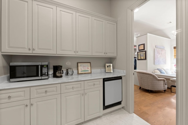 kitchen featuring white cabinetry, light stone countertops, fridge, and light hardwood / wood-style floors