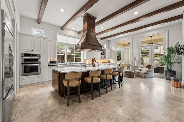 kitchen with a breakfast bar, white cabinets, stainless steel appliances, beam ceiling, and a spacious island