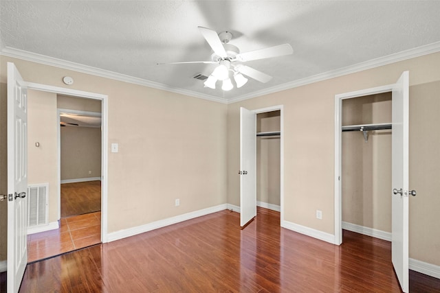 unfurnished bedroom with crown molding, hardwood / wood-style flooring, ceiling fan, and two closets