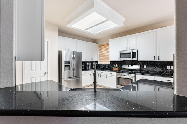 kitchen with appliances with stainless steel finishes, white cabinets, backsplash, and dark stone counters