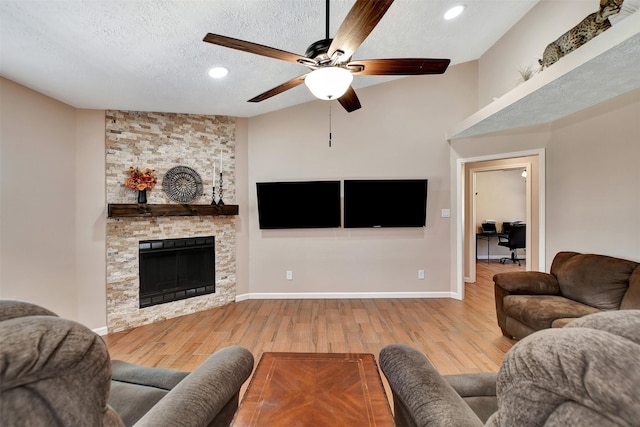 living room featuring lofted ceiling, ceiling fan, a fireplace, a textured ceiling, and light wood-type flooring