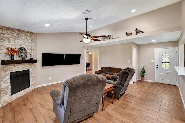 living room featuring ceiling fan, a stone fireplace, and a textured ceiling