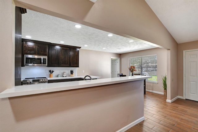 kitchen with lofted ceiling, sink, stainless steel appliances, dark brown cabinetry, and kitchen peninsula