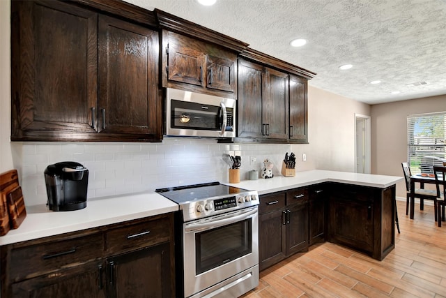 kitchen featuring dark brown cabinetry, a textured ceiling, kitchen peninsula, stainless steel appliances, and backsplash