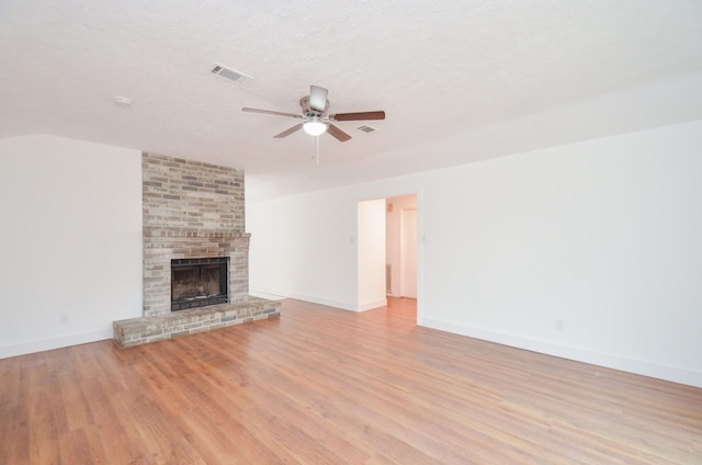 unfurnished living room featuring a fireplace, lofted ceiling, ceiling fan, light hardwood / wood-style floors, and a textured ceiling