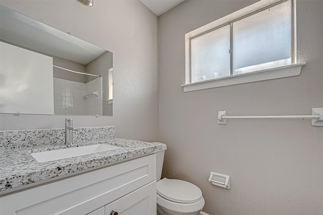 bathroom with vanity, tiled shower, and toilet