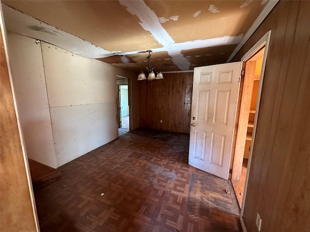 unfurnished room featuring a notable chandelier, dark parquet flooring, and wooden walls