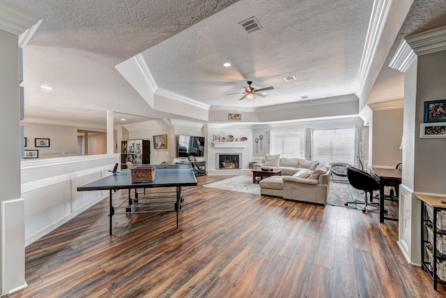 living room with a fireplace, ornamental molding, ceiling fan, dark wood-type flooring, and a textured ceiling