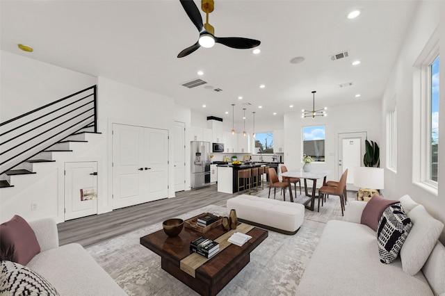 living room featuring light hardwood / wood-style flooring, sink, ceiling fan with notable chandelier, and plenty of natural light