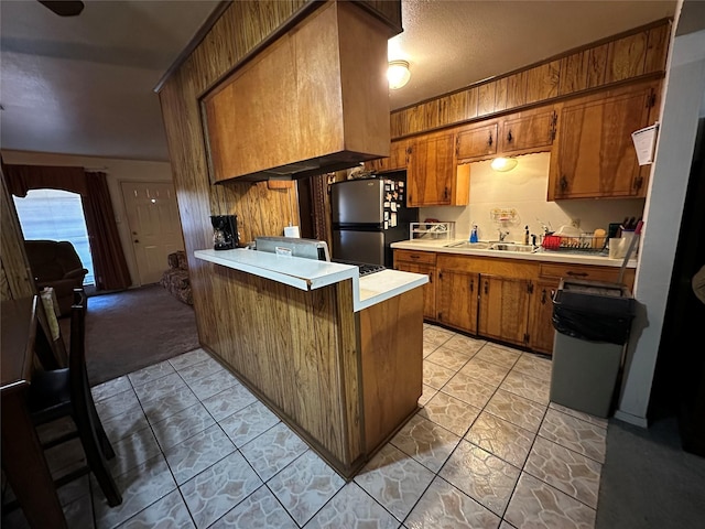 kitchen with stainless steel fridge, kitchen peninsula, sink, and wood walls