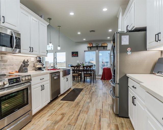 kitchen with pendant lighting, light hardwood / wood-style flooring, appliances with stainless steel finishes, white cabinets, and decorative backsplash