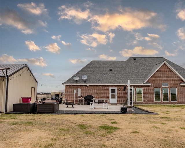 back house at dusk with a hot tub, a patio, and a yard