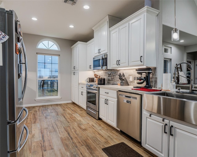 kitchen featuring sink, white cabinetry, stainless steel appliances, decorative backsplash, and light wood-type flooring