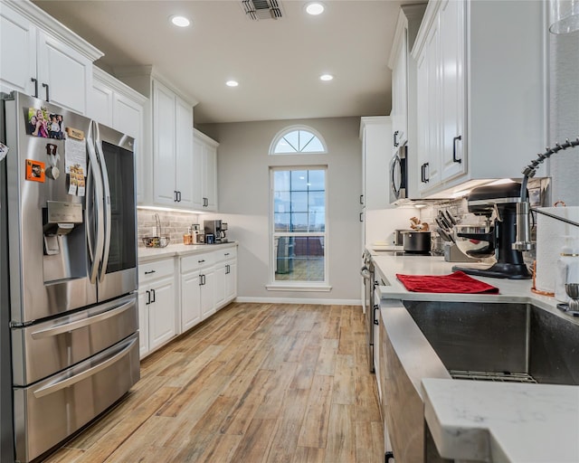 kitchen featuring white cabinetry, backsplash, stainless steel appliances, light stone countertops, and light wood-type flooring