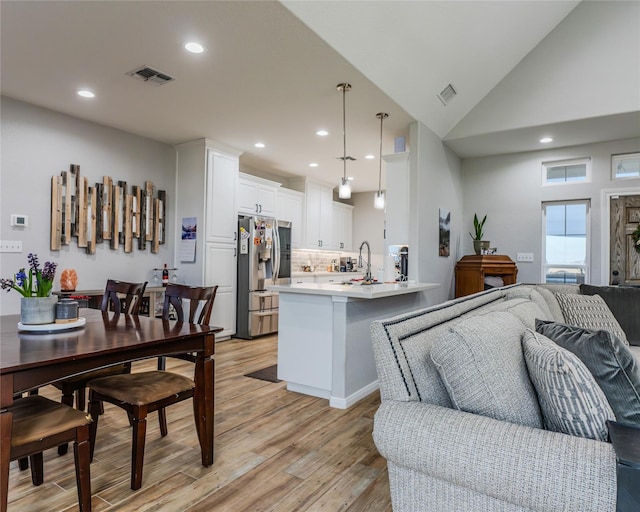 kitchen featuring stainless steel refrigerator with ice dispenser, light hardwood / wood-style floors, white cabinets, decorative light fixtures, and kitchen peninsula