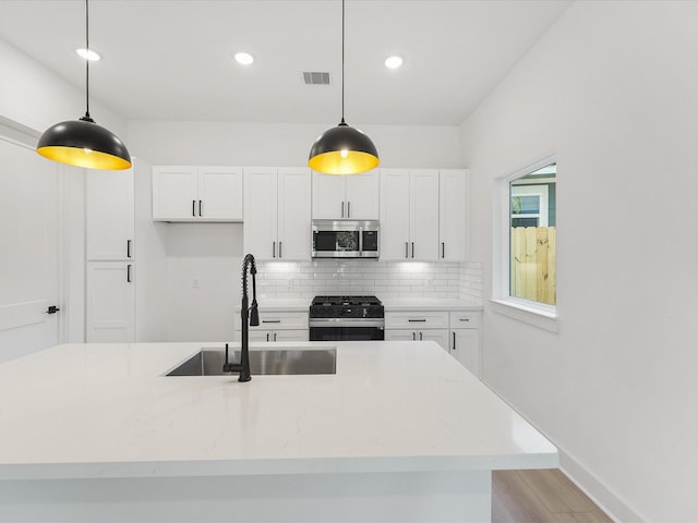 kitchen featuring appliances with stainless steel finishes, pendant lighting, sink, white cabinets, and decorative backsplash