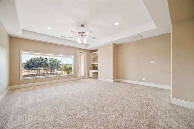 unfurnished living room with ceiling fan, a tray ceiling, and light carpet