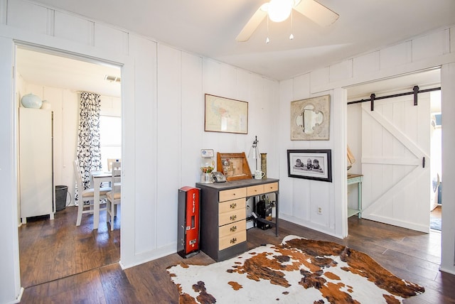 interior space with ceiling fan, a barn door, dark wood finished floors, and a decorative wall