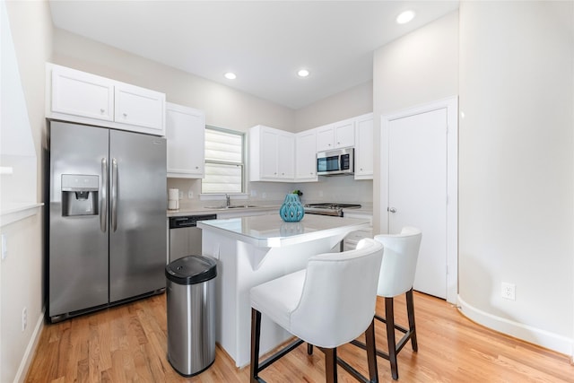 kitchen featuring a breakfast bar area, a center island, light hardwood / wood-style flooring, stainless steel appliances, and white cabinets