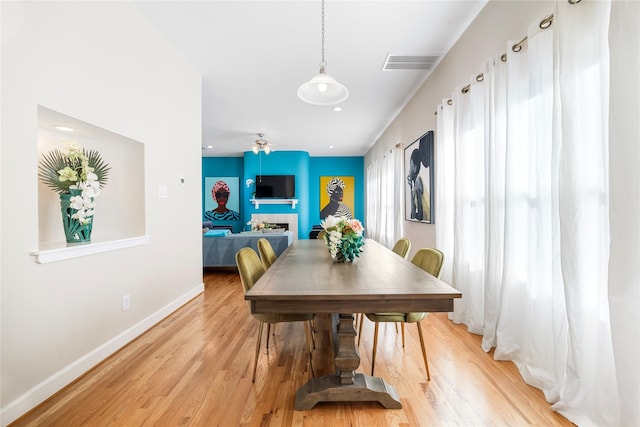 dining room featuring ceiling fan, a fireplace, and light hardwood / wood-style floors