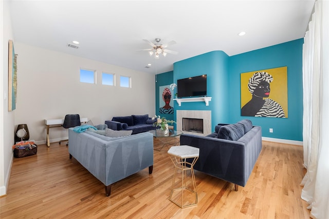 living room featuring ceiling fan, a tile fireplace, and light hardwood / wood-style flooring