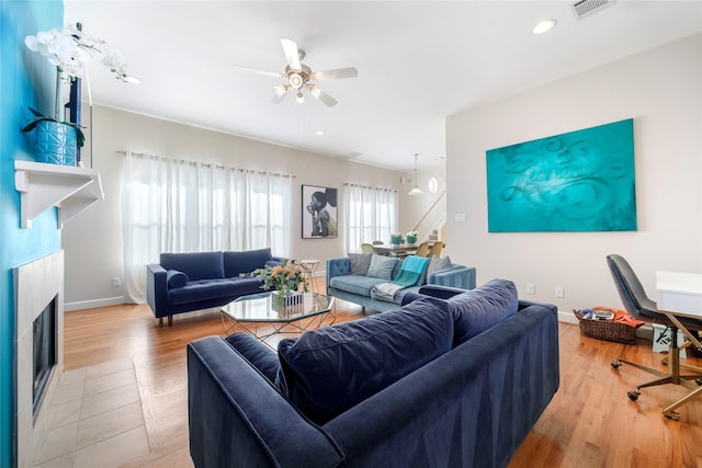 living room featuring ceiling fan, wood-type flooring, and a tile fireplace