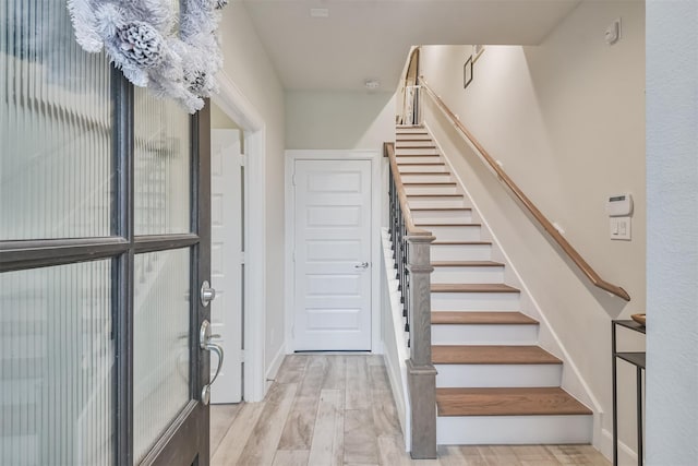 foyer with light wood finished floors, baseboards, and stairway