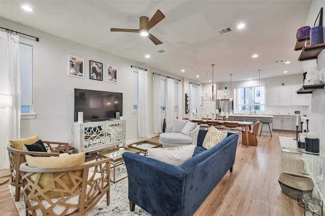 living area featuring ceiling fan with notable chandelier, light wood finished floors, visible vents, and recessed lighting