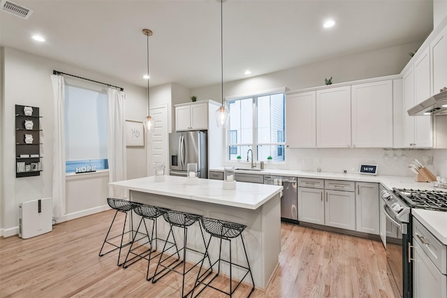 kitchen featuring white cabinetry, decorative light fixtures, light wood-type flooring, a kitchen island, and stainless steel appliances