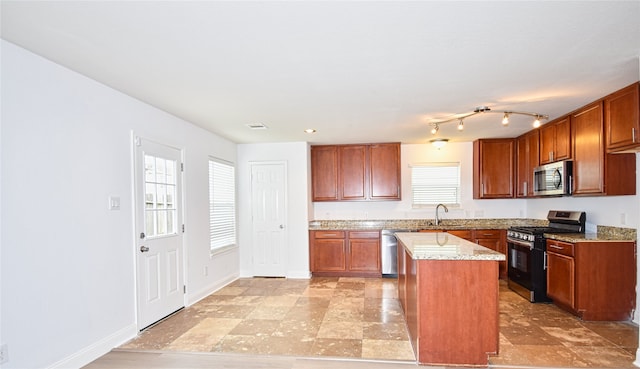 kitchen featuring light stone countertops, appliances with stainless steel finishes, a center island, and sink