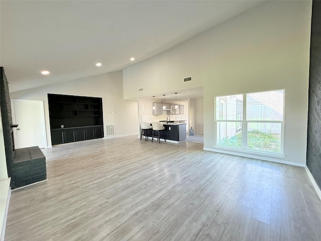 unfurnished living room featuring sink, light hardwood / wood-style flooring, and high vaulted ceiling