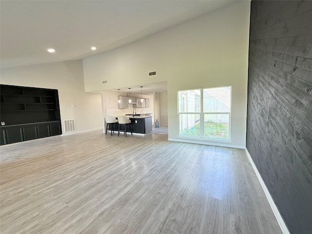 unfurnished living room with sink, high vaulted ceiling, and light hardwood / wood-style flooring