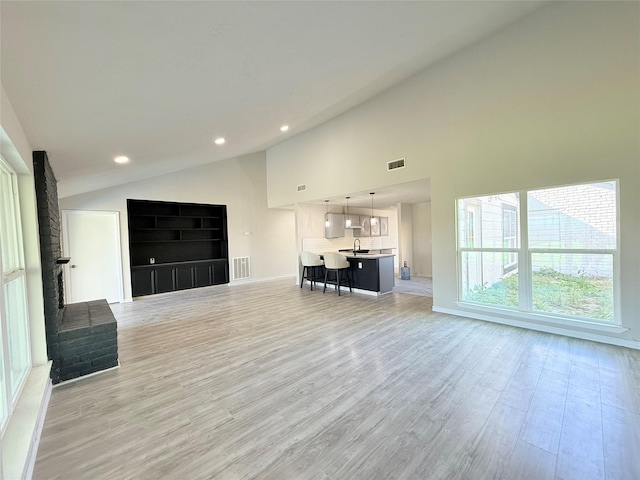 unfurnished living room with sink, light hardwood / wood-style flooring, and high vaulted ceiling